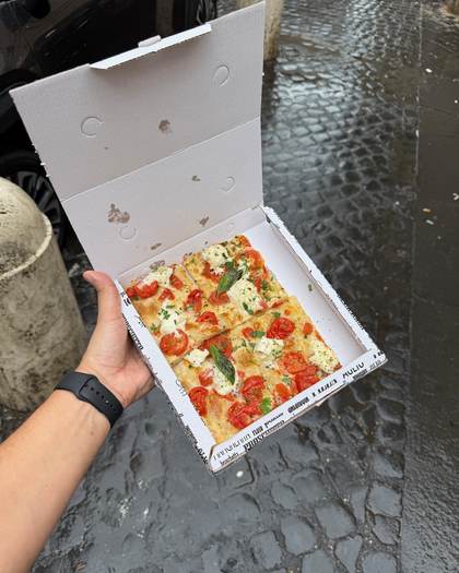 Pizza al taglio numa caixa, na calçada molhada de Roma
