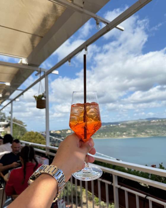 Taça de spritz erguida em terraço com vista para o lago